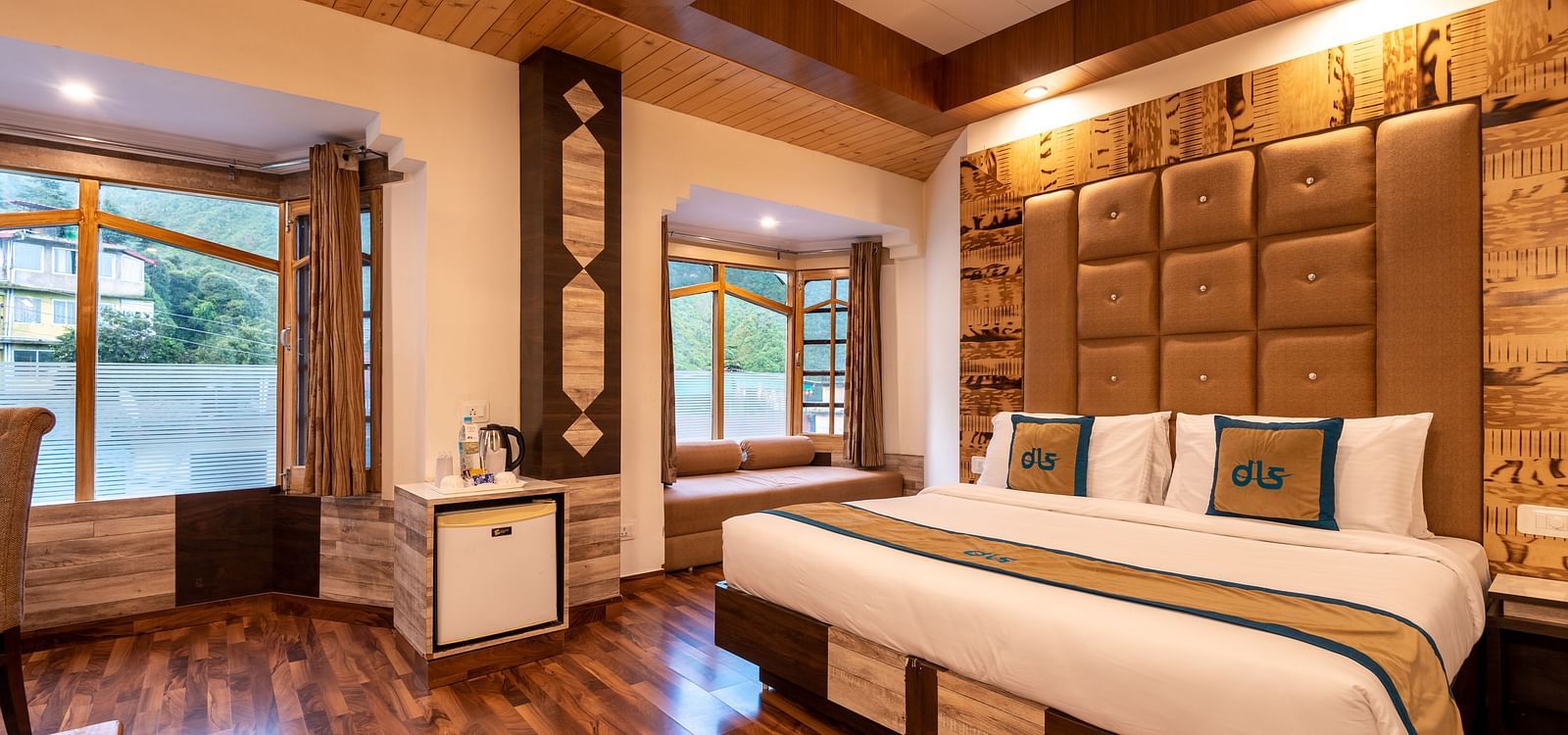 A hotel room in Bhagsunag featuring a large bed, wooden floors, a wooden ceiling, and windows with a view - DLS Meghavan Resort